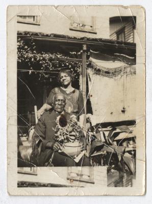 A man with a plant in his lap and a woman standing behind